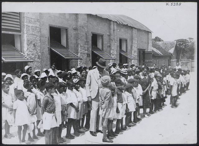 'Poor children of Bridgetown, Barbados, receive free lunch provided daily by the Childrens' Goodwill League, under the chairmanship of John Beckles, who is chatting with the children'. Photo: Flickr/Official Barbados photograph compiled by Central Office of Information.